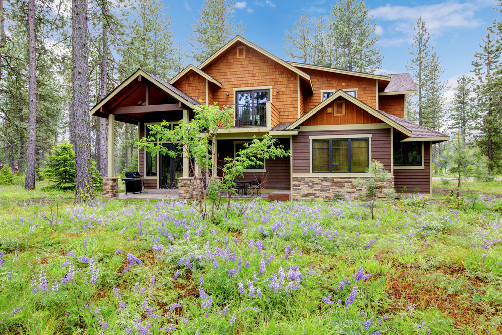 Mountain,Cabin,Home,Wood,Exterior,With,Forest,And,Flowers. Featured image showing a mountain home with natural landscaping and wildflowers.