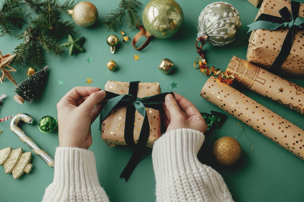 Merry,Christmas!,Hands,Wrapping,Stylish,Christmas,Gift,,Golden,Wrapping,Paper, Featured image showing hands wrapping stylish christmas gift, golden wrapping paper, green ribbon and festive decorations on green background.