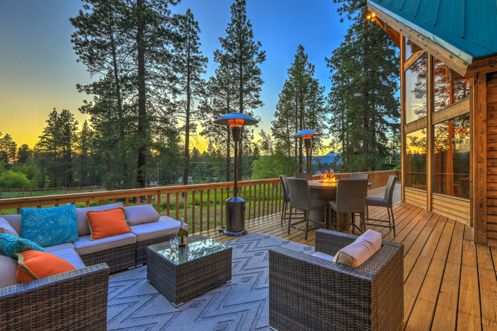 Beautiful,Chalet,Cider,Home,Exterior,During,Evening,With,New,Deisgn Featured image showing a deck of a mountain home with outdoor furniture a fire table, heat lamps and plenty of cosy pillows and blankets.
