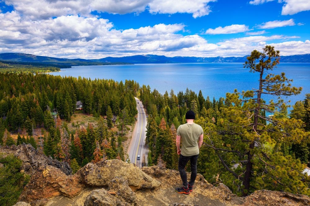 Hiker,Enjoying,The,View,Of,Lake,Tahoe,From,The,Eagle Featured image showing a man looking at Lake Tahoe from Eagle Rock in California, with Sierra Nevada Mountains in the background.